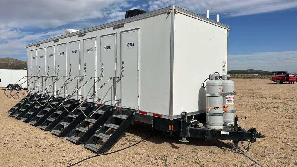 Eight station shower trailer with steps and a rail at every door on bare desert ground, propane cylinders on the tongue