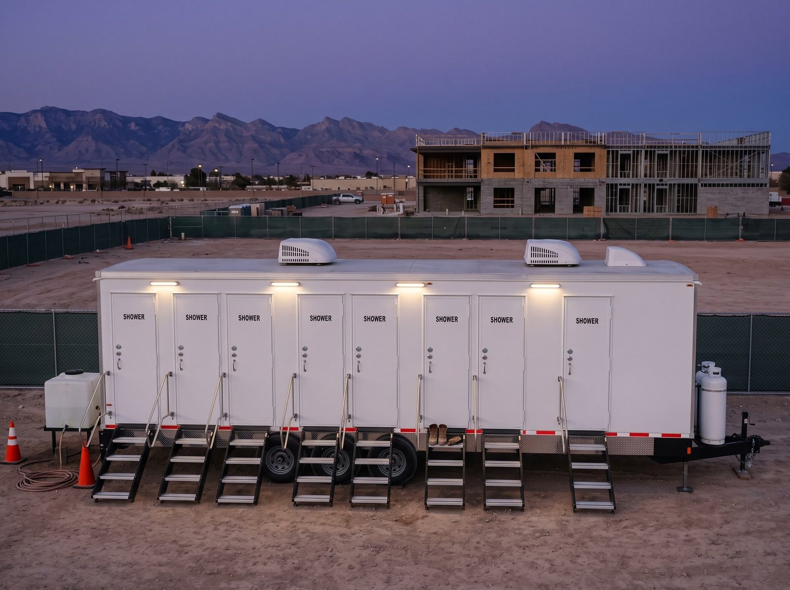 Eight station shower trailer at dusk on a fenced construction lot in Enterprise, Las Vegas, steps and a rail at every door