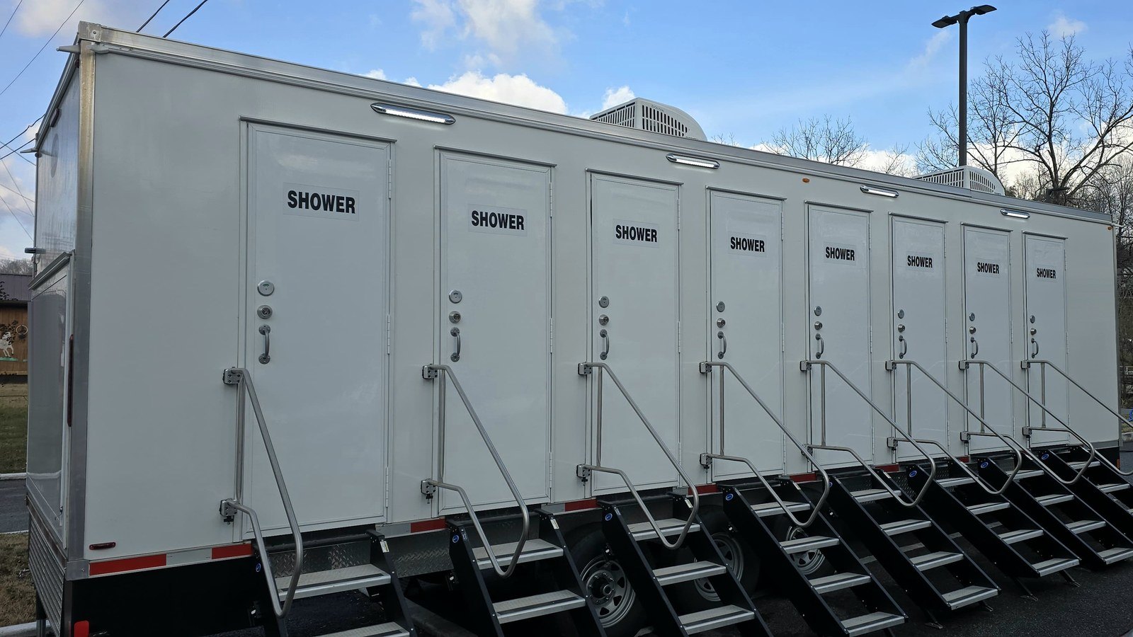 Eight station shower trailer on a paved lot, every door labeled SHOWER with its own steps and rail, roof air units running on a clear morning