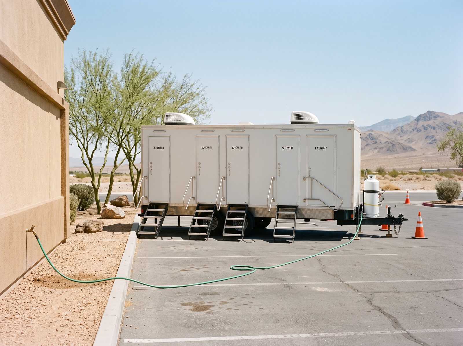 Four stall shower trailer on a paved Henderson lot with a hose running from a hose bib on a stucco wall