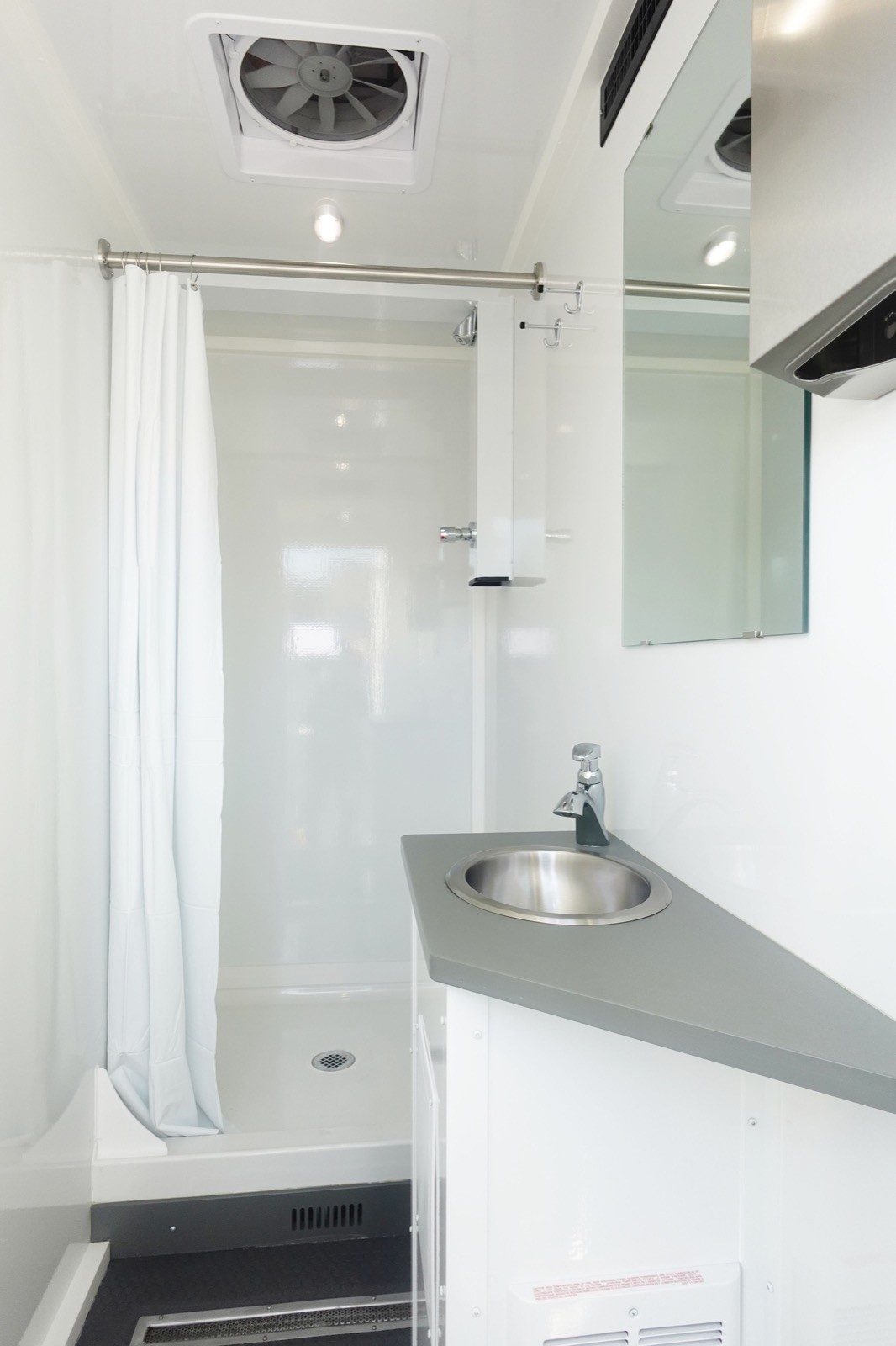 Inside a private shower trailer stall: curtain, shower, a vanity with a round stainless sink and a mirror