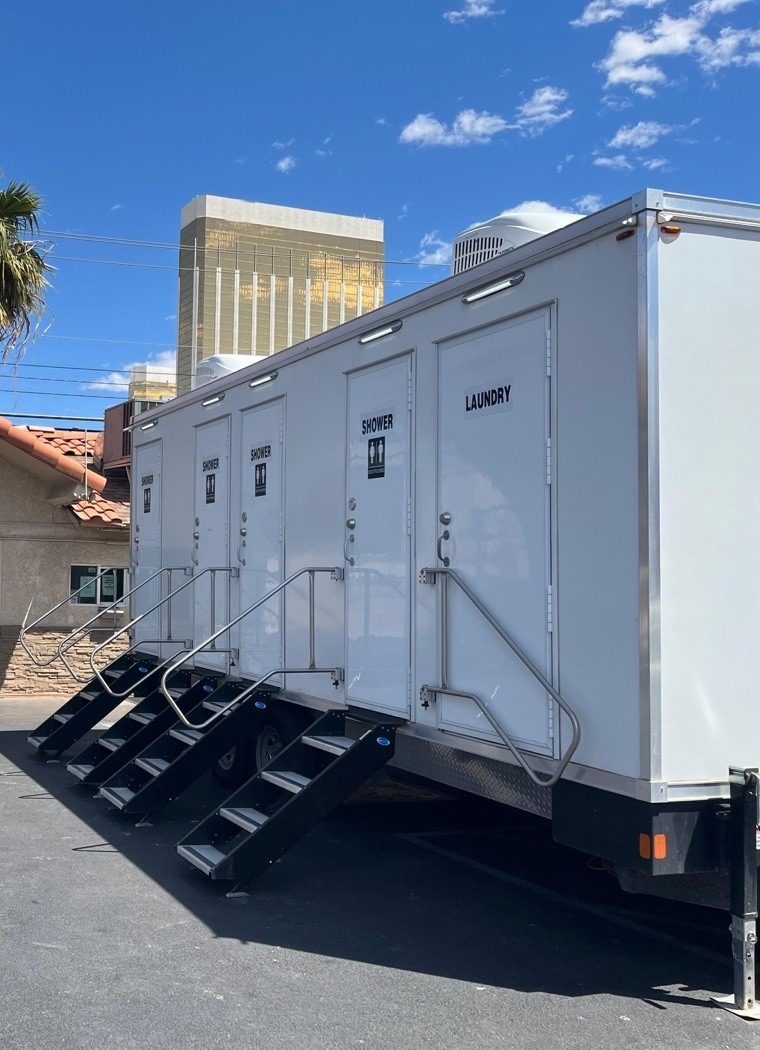 Shower and laundry combo trailer staged in a paved lot with a gold resort tower on the Las Vegas Strip behind it