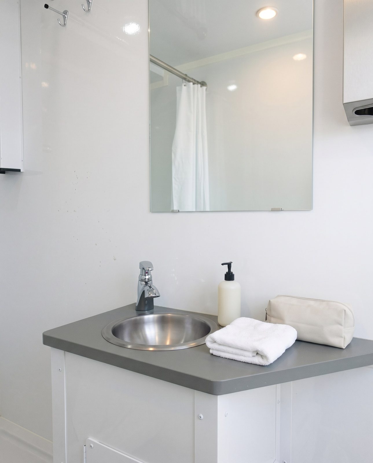 Grey vanity counter with a round stainless sink and a folded towel inside a private shower trailer stall